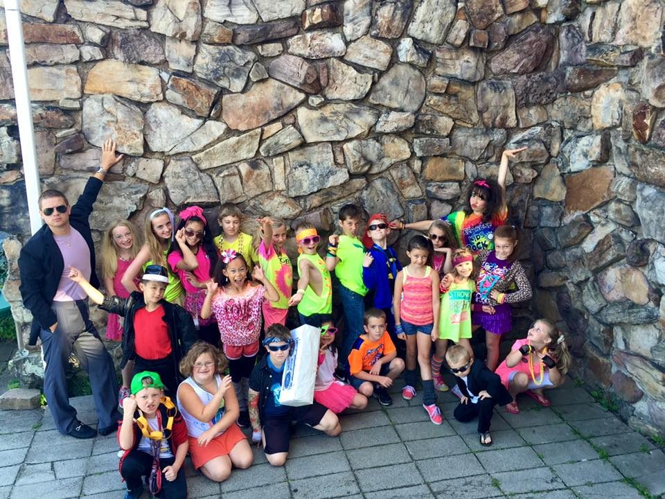 A big group of kids in bright colors posing together in front of the stone castle wall