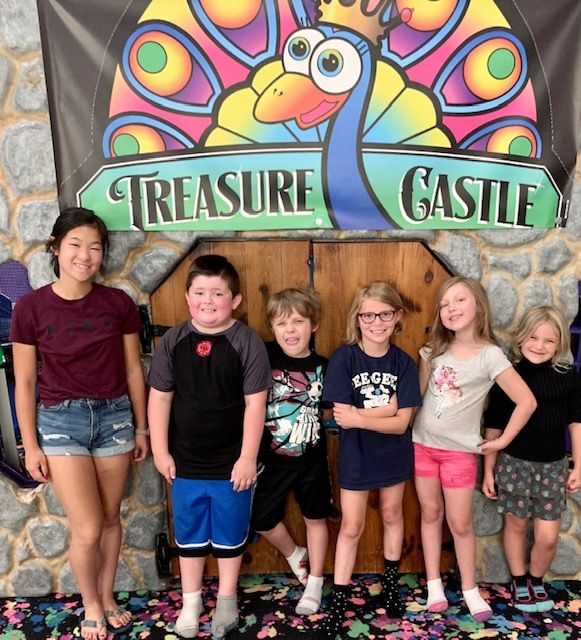 Kids smiling in front of the Treasure Castle peacock sign inside the playland